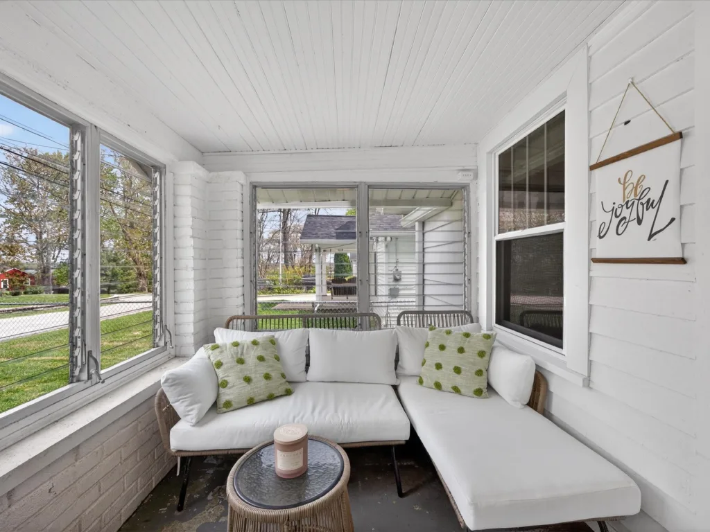 Bright enclosed sunroom with white walls, a cushioned sectional and windows on three sides in a Bloomington bungalow